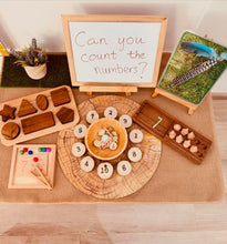 Load image into Gallery viewer, A styled collection of wooden educational toys and learning aids arranged on a burlap runner in front of a whiteboard that reads 'Can you count the numbers?'. The set includes a wooden number counting board with round wooden number discs, a wooden shape sorting tray, a wooden bead abacus, a wooden number 7 abacus, a small wooden color-matching board, and a small potted plant.
