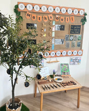 Load image into Gallery viewer, A styled children's maths display in a classroom or playroom, featuring a large burlap 'Maths Wall' with number cutouts, equations, and educational posters, alongside a small wooden table with counting toys and a potted tree.
